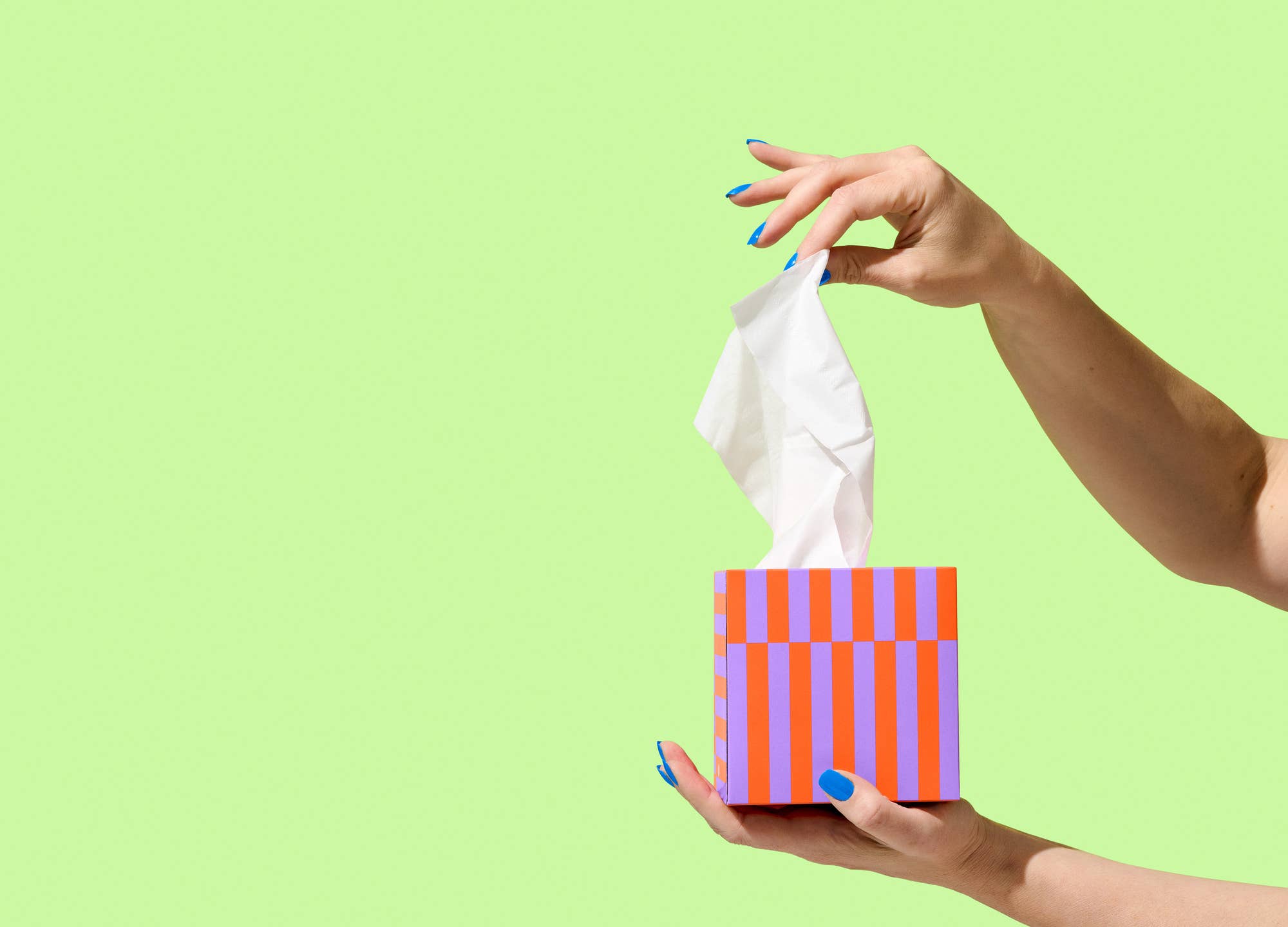 Hand pulling a tissue from a striped box against a lime green background.
