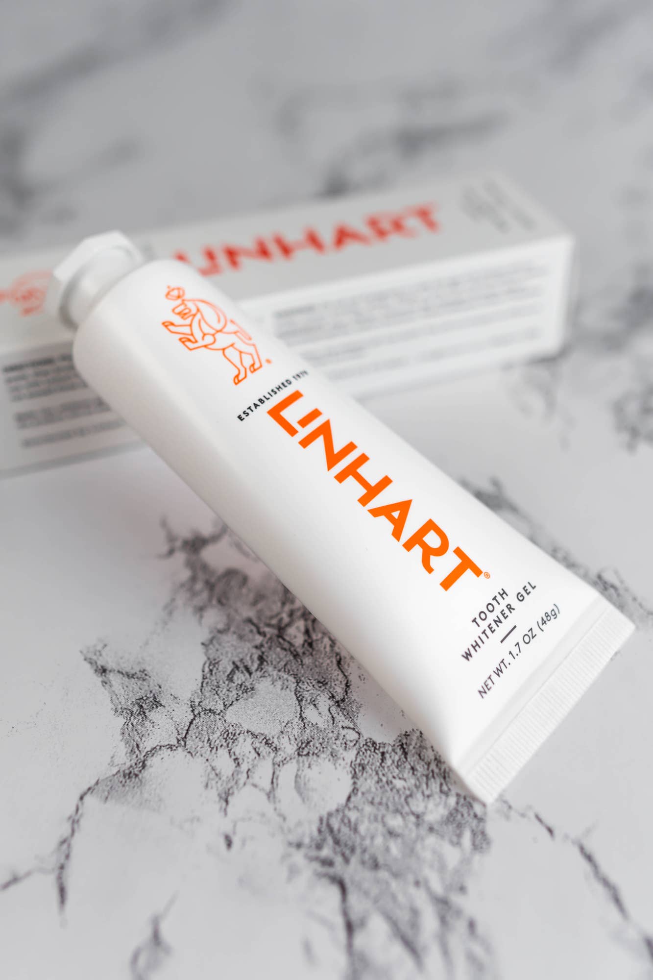 Linhart Tooth Whitener Gel tube with orange logo on marble background.