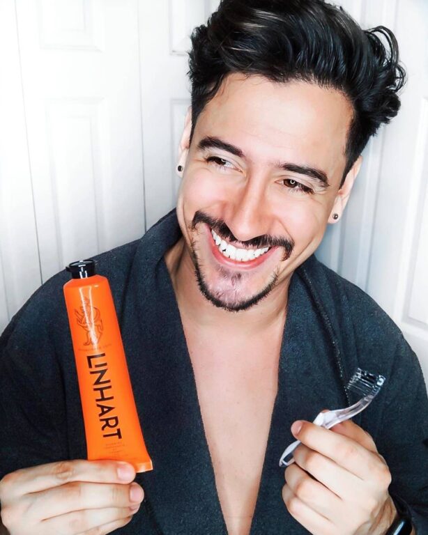 Man in robe smiles, holding orange toothpaste tube and toothbrush.