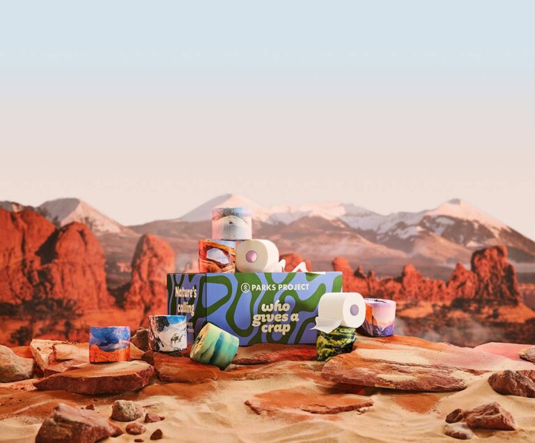 Toilet paper rolls with nature-themed designs stacked on a box in a desert landscape.