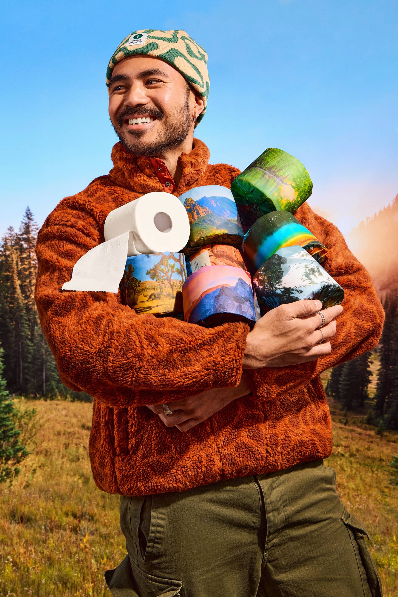 Man in orange fleece holding toilet paper rolls with scenic landscape designs.